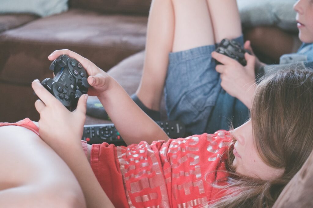 Kinder spielen Videospiele mit Controllern, während sie sich auf die Sofas legen