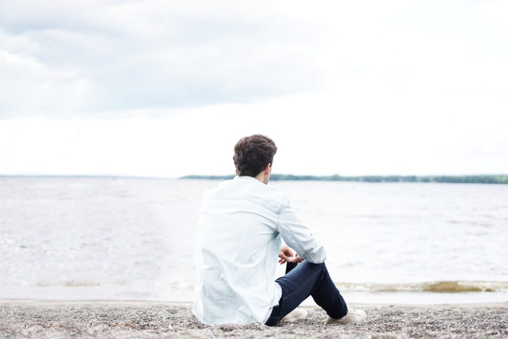 Eine Person in einem weißen Hemd und einer dunkelblauen Hose sitzt am Strand